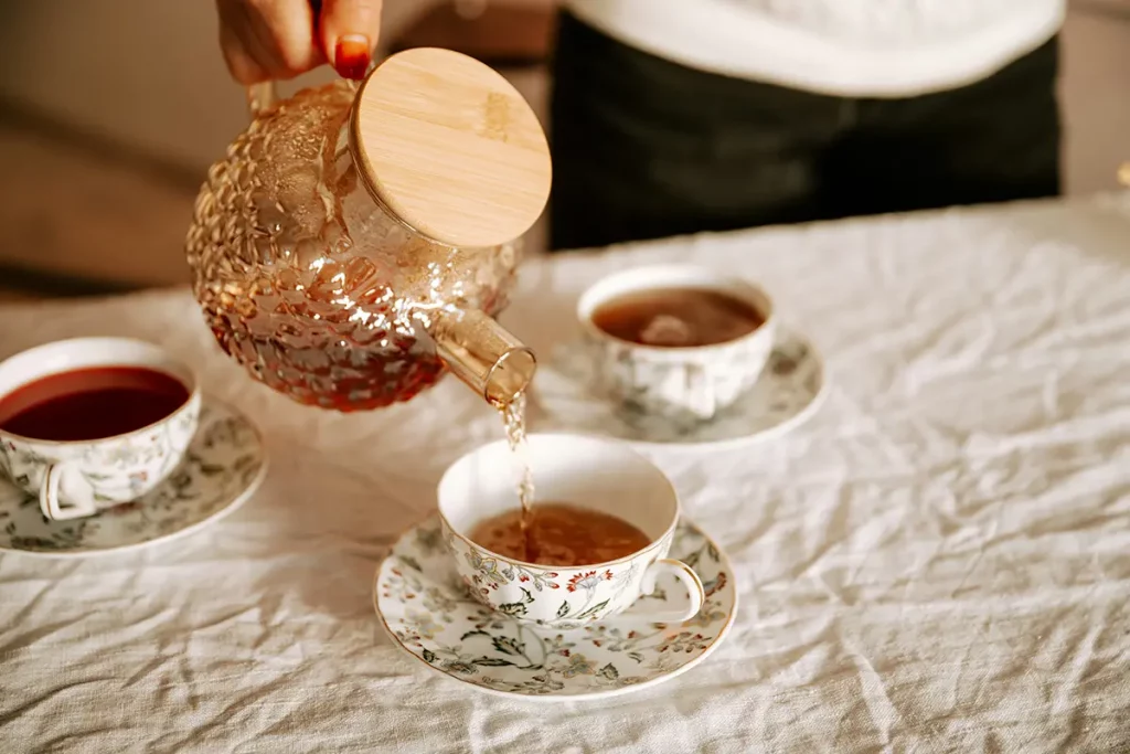 Une femme verse du thé à la menthe depuis une théière en verre, avec un joli filet de mousse