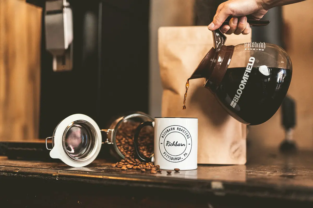 Café versé dans une tasse à côté d’un bocal ouvert et de grains de café.