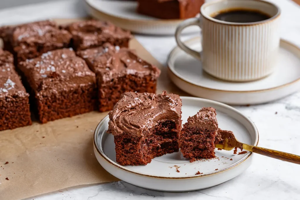 Parts de gâteau au chocolat avec glaçage, servies à côté d’une tasse de café noir.